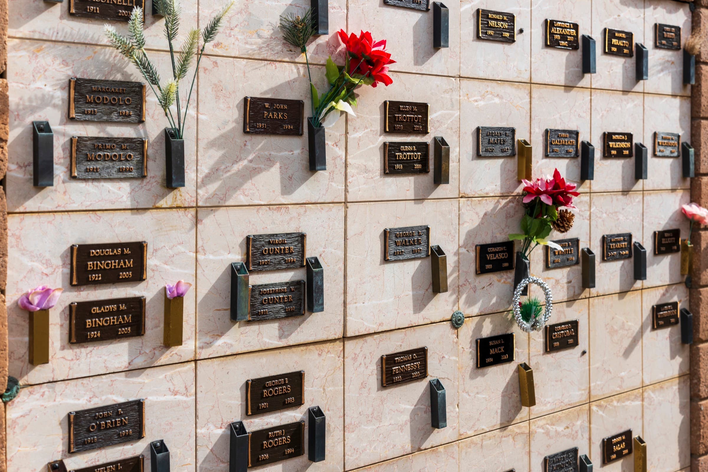 A sunlit niche wall with floral tributes